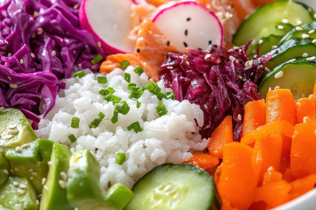 Colorful vegan poke bowl featuring fresh vegetables like cucumber, radish, and purple cabbage, topped with sesame seeds.