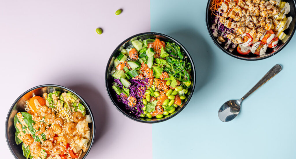 Drei bunte Schüsseln mit frischem Gemüse, Reis, Tofu und Garnelen auf Pastellflächen